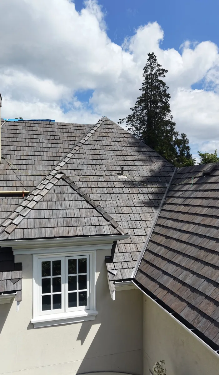 Close-up of installed Brava composite cedar shake showing hand-split texture, hip cap and dormer detail